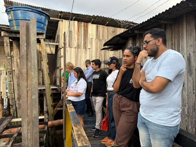 Na imagem pessoas observam casas de madeira da Vila da Barca