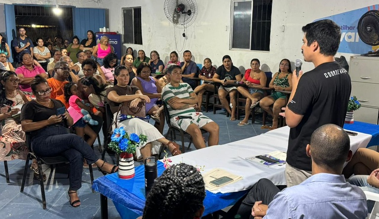 Na imagem pessoas sentadas numa sala ouvindo um homem representante do ministério.