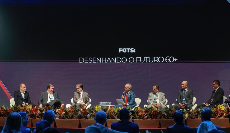 Na imagem ministro ao lado de palestrantes do encontro nacional da construção civil, ele discursa para plateia.