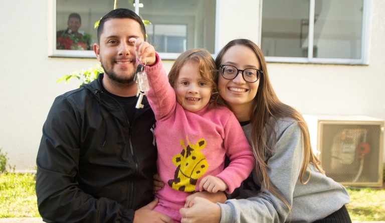 Na imagem família sorrindo com criança segurando chave da casa p´rópria