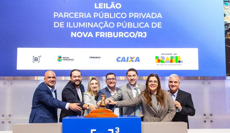 Na imagem pessoas posam para foto durante leilão de iluminação pública, na B3, três pessoas batem martelo.