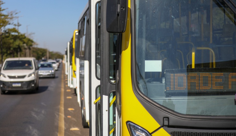 Na imagem ônibus do transporte público enfilerados, ao lado carros parados.