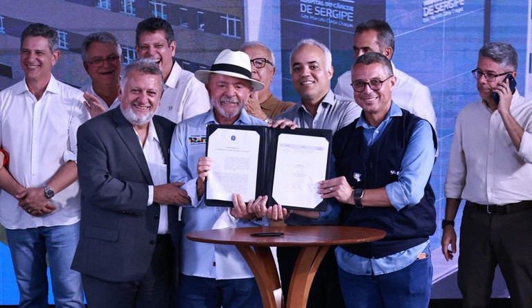 Na foto o ministro das cidades junto ao presidente da república e outras autoridades exibindo o documento