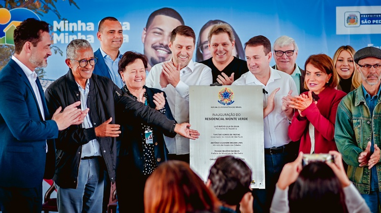 Na imagem pessoas participam de evento de entrega de casas