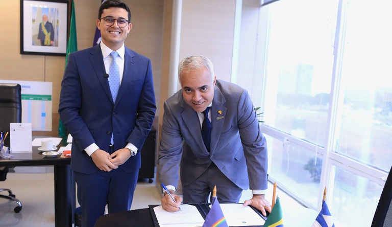 Na imagem ministro e dois homens posam para foto segurando documento de assinaturas de obras de drenagem