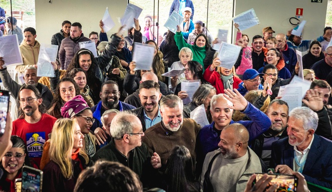 Na imagem ministro das cidades posa para foto com beneficiários do minha casa minha segurando documento da casa propria