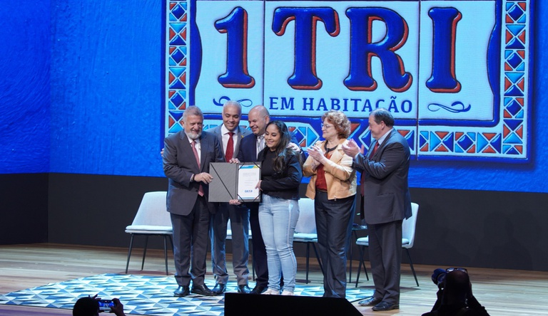 Na imagem ministro das cidades posa para foto com representantes do governo e beneficiária do programa Minha Casa, Minha Vida