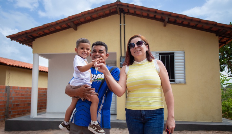 Na imagem um homem, uma mulher e uma criança posam para foto segurando chave da casa propria.