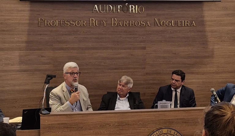 Na imagem embaixador Antônio da Costa e Silva discursa no evento economia circular e descarbonização das cidades, ao lado dois homens sentados.
