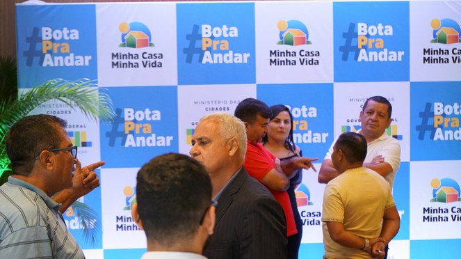 Na foto pessoas conversando a frente do banner do Bota pra Andar