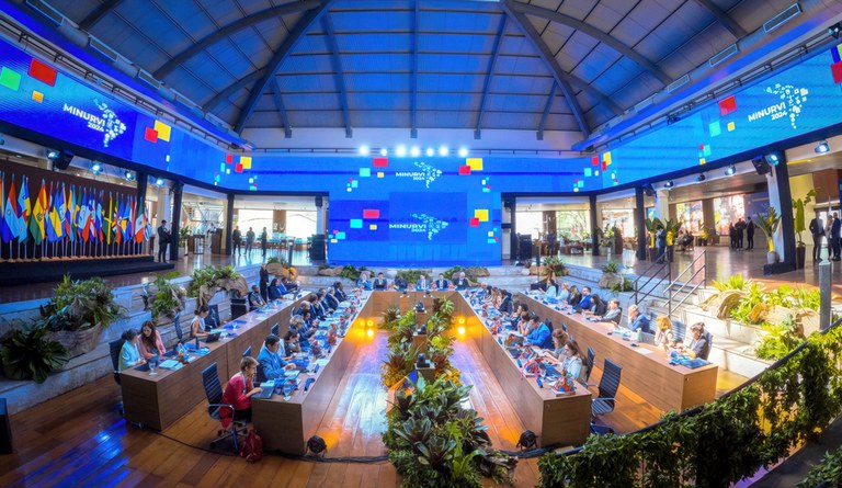 Na foto vista geral do pavilhão com quatro fileiras de mesas e seus ocupantes a frente de computadores
