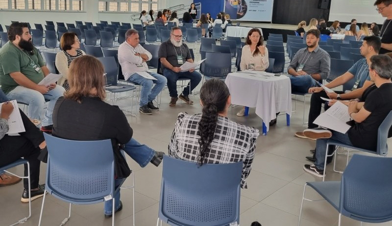 Na foto grupos de pessoas sentadas em uma sala conversando