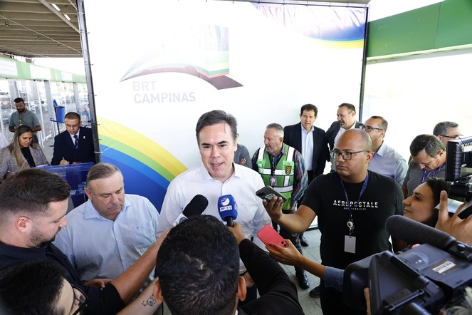 Homem branco, veste roupa social branca em frente a microfones de jornalistas.