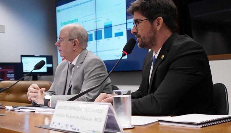 Dois homens sentados em frente ao microfone dando entrevista.
