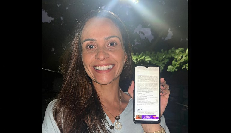 Mulher sorrindo segura celular com foto do primeiro contrato do Minha Casa, Minha Vida - Classe Média