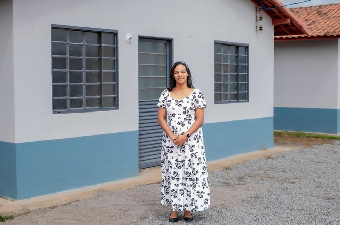 Mulher sorrindo em frente a uma casa do programa Minha Casa, Minha Vida.