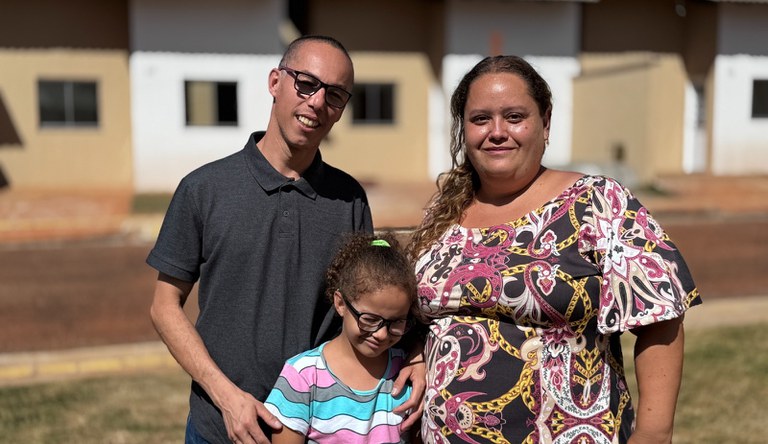 Casal e uma criança em frente a sua nova casa do MCMV.