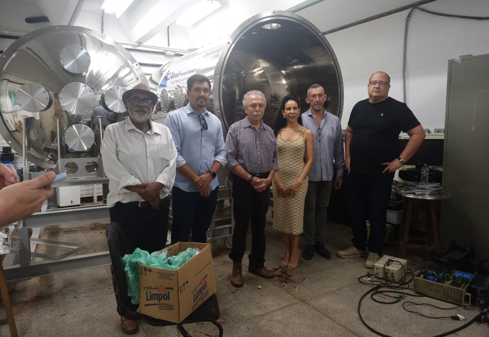 Prof. Galvão em frente à câmera de vácuo do Laboratório de Física de Plasmas acompanhado de professores e do diretor do Instituto de Física.