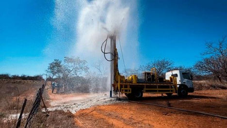 Perfuração de poço tubular com equipamento em operação em área rural.