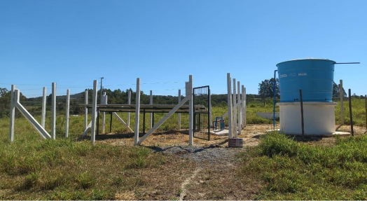 Poço com reservatório e estrutura cercada em área rural.