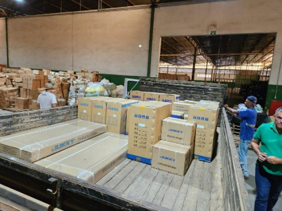 Caixas empilhadas em caminhão dentro de galpão com trabalhadores ao redor.