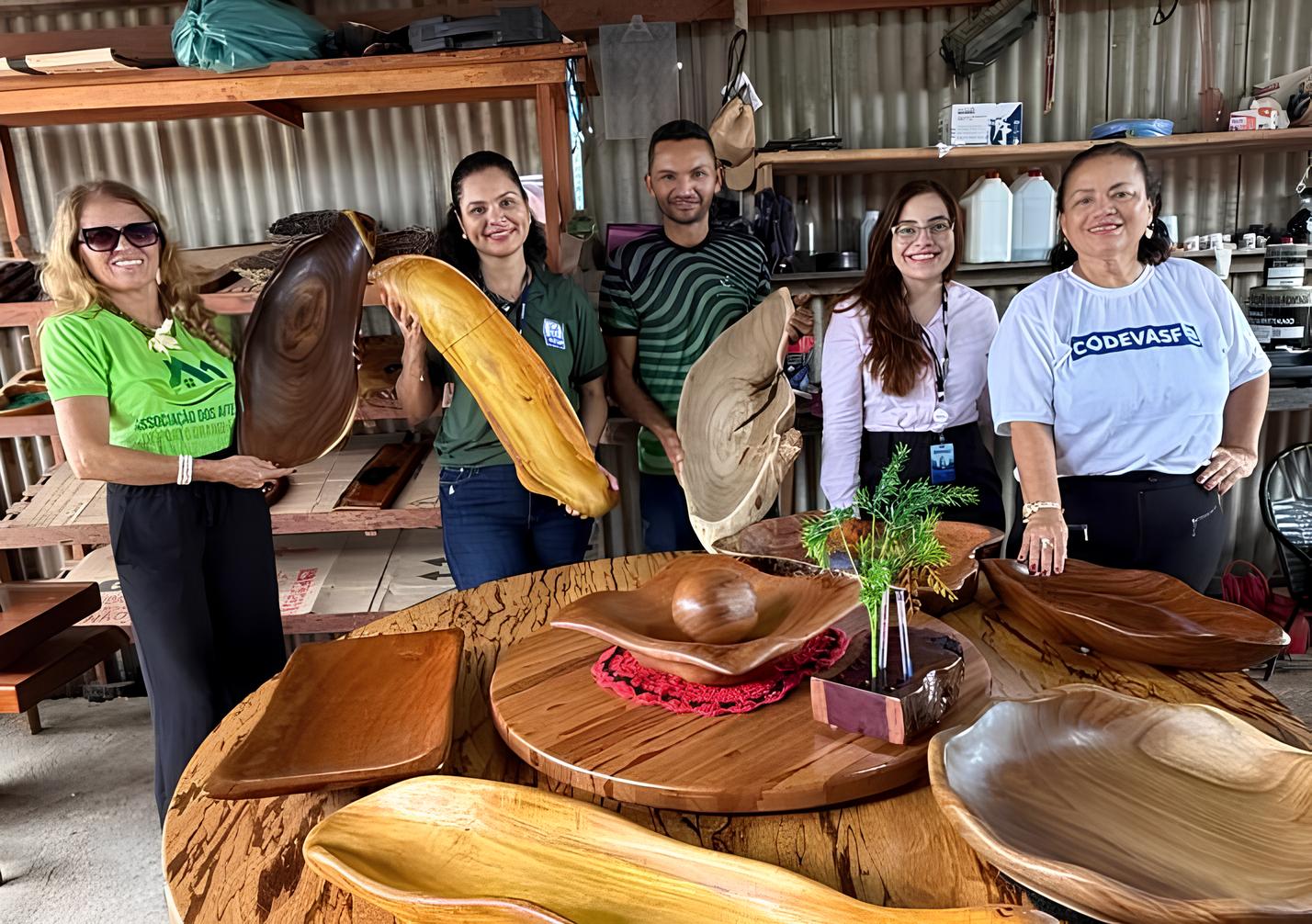 Cinco pessoas posam ao redor de mesa com peças artesanais de madeira.