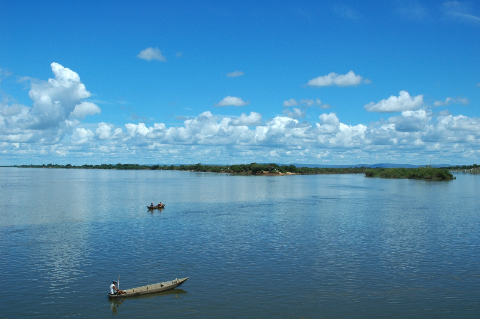 Canoas em rio com vegetação nas margens e céu com nuvens brancas