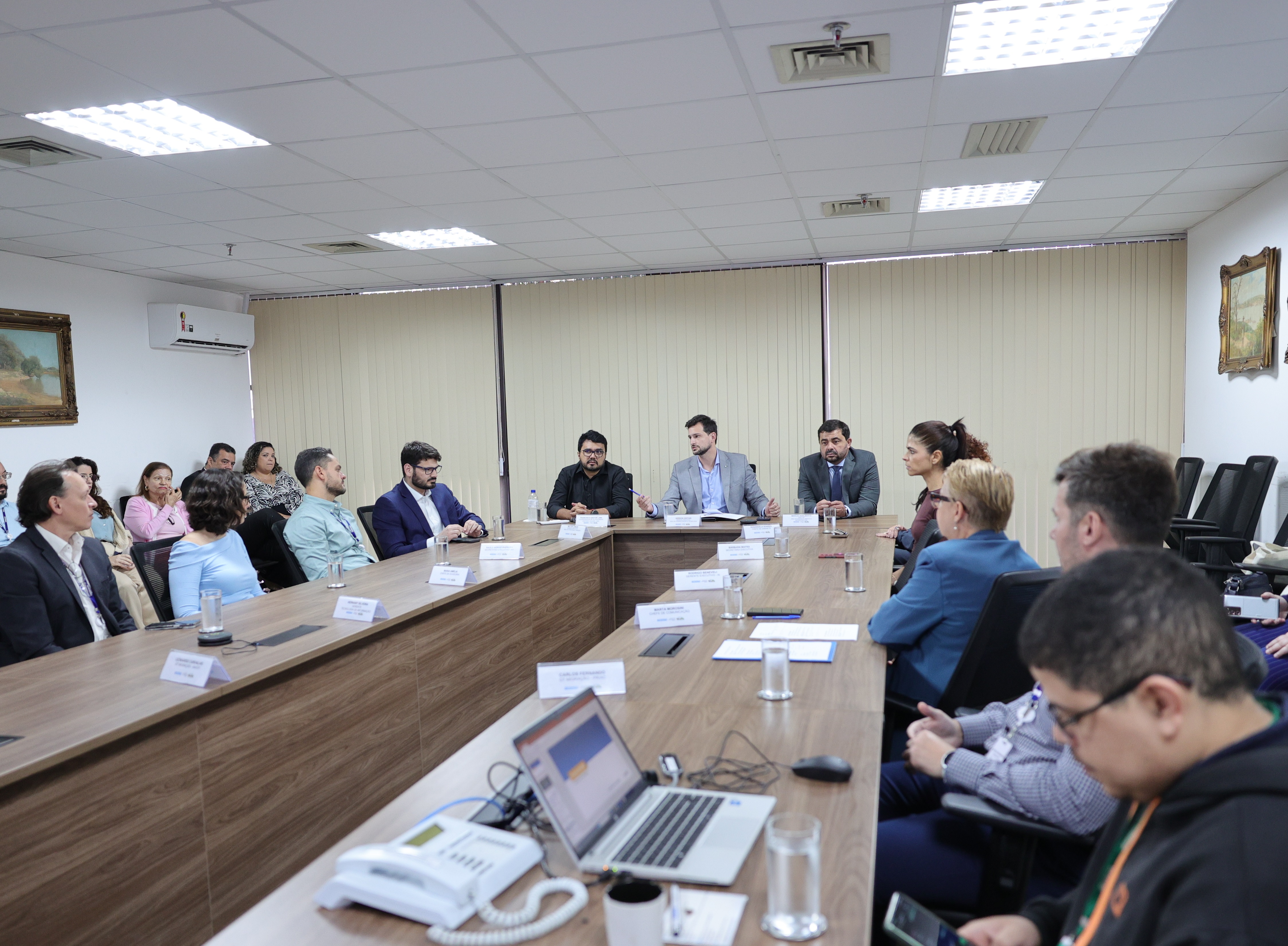 Grupo de pessoas reunidas em mesa de conferência durante reunião institucional.
