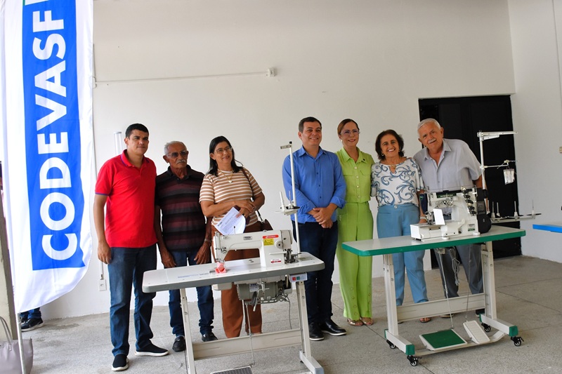 Equipe e beneficiários ao lado de máquinas de costura em ação de entrega.