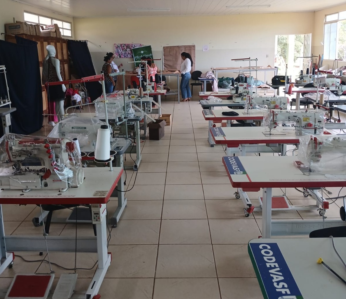 Sala ampla com máquinas de costura industriais e pessoas ao fundo