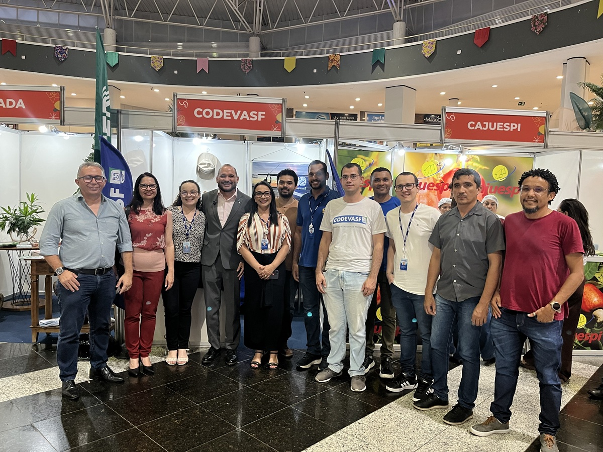 Grupo de pessoas posando sorridentes em frente a estandes com letreiros da Codevasf e Cajuespi.