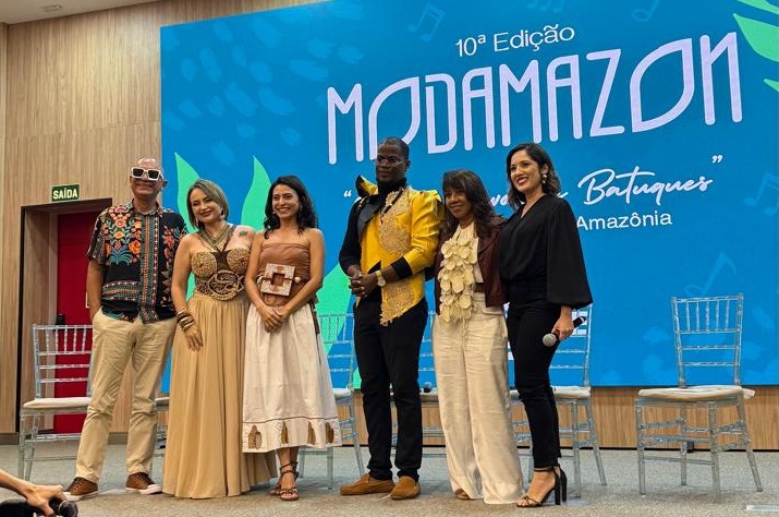 Seis pessoas posam em um palco à frente de um painel azul escrito "10ª Edição Modamazon".