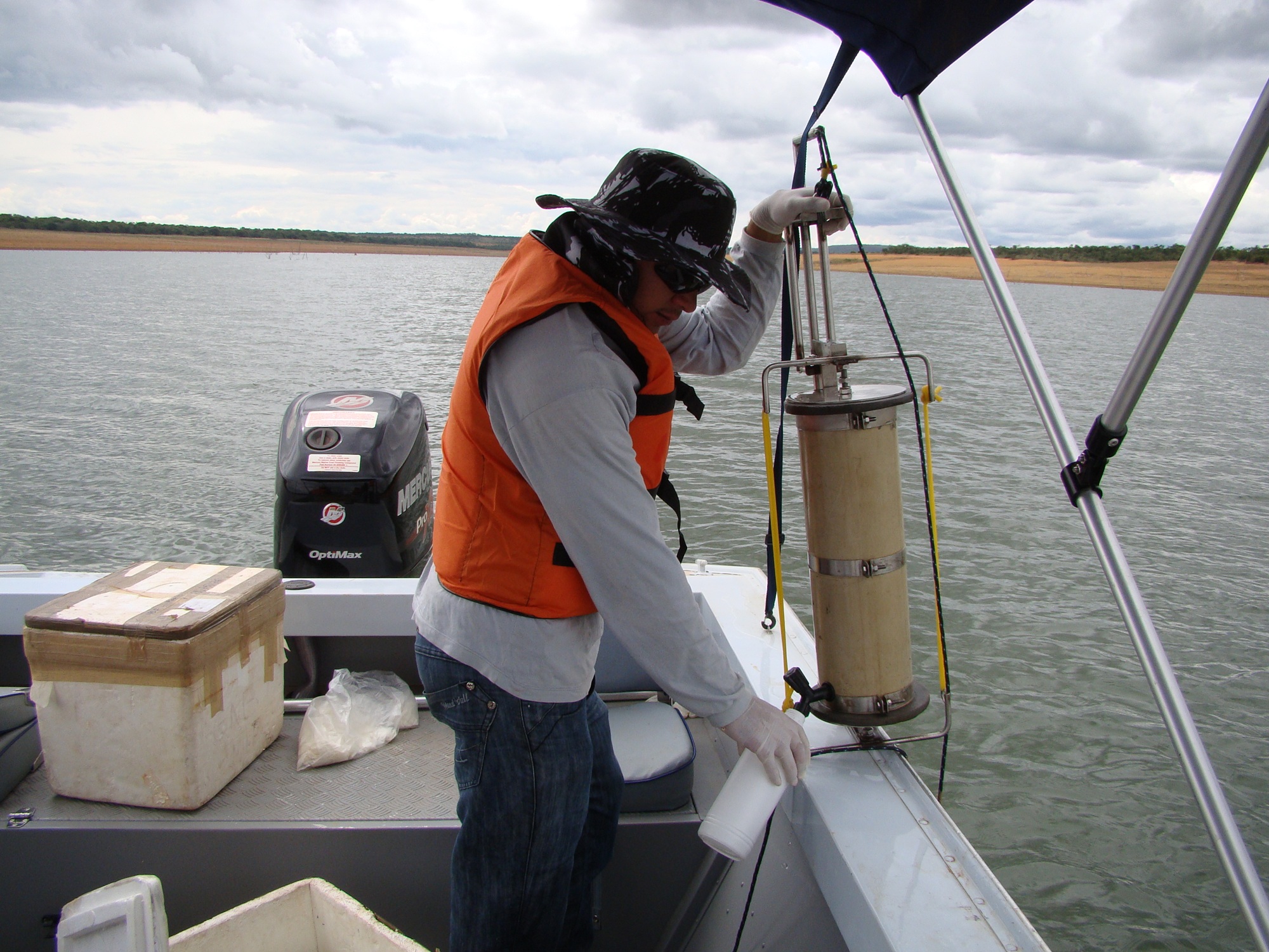 Homem de colete salva-vidas manuseia equipamento cilíndrico de coleta de água a bordo de um barco
