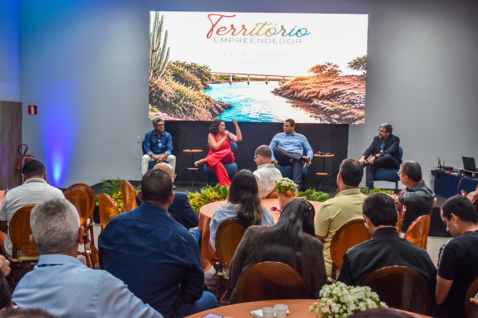 Público acompanha debate em palco durante seminário com telão ao fundo