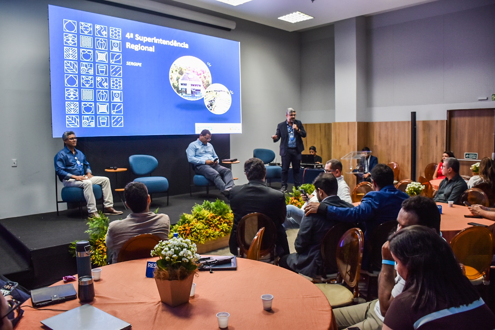 Participantes acompanham apresentação em seminário realizado em auditório com telão