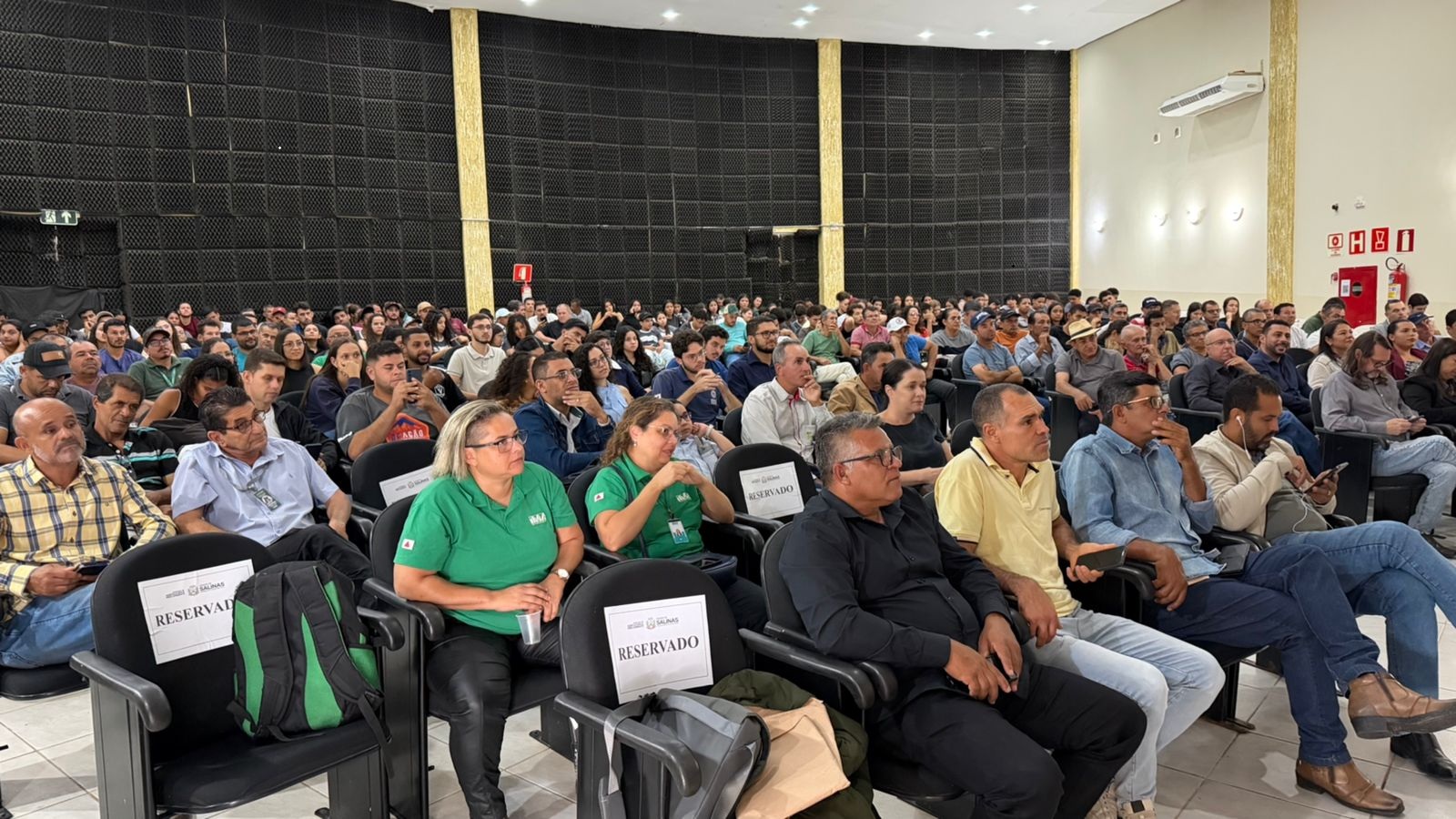 Público diverso assistindo palestra em auditório com cadeiras reservadas.