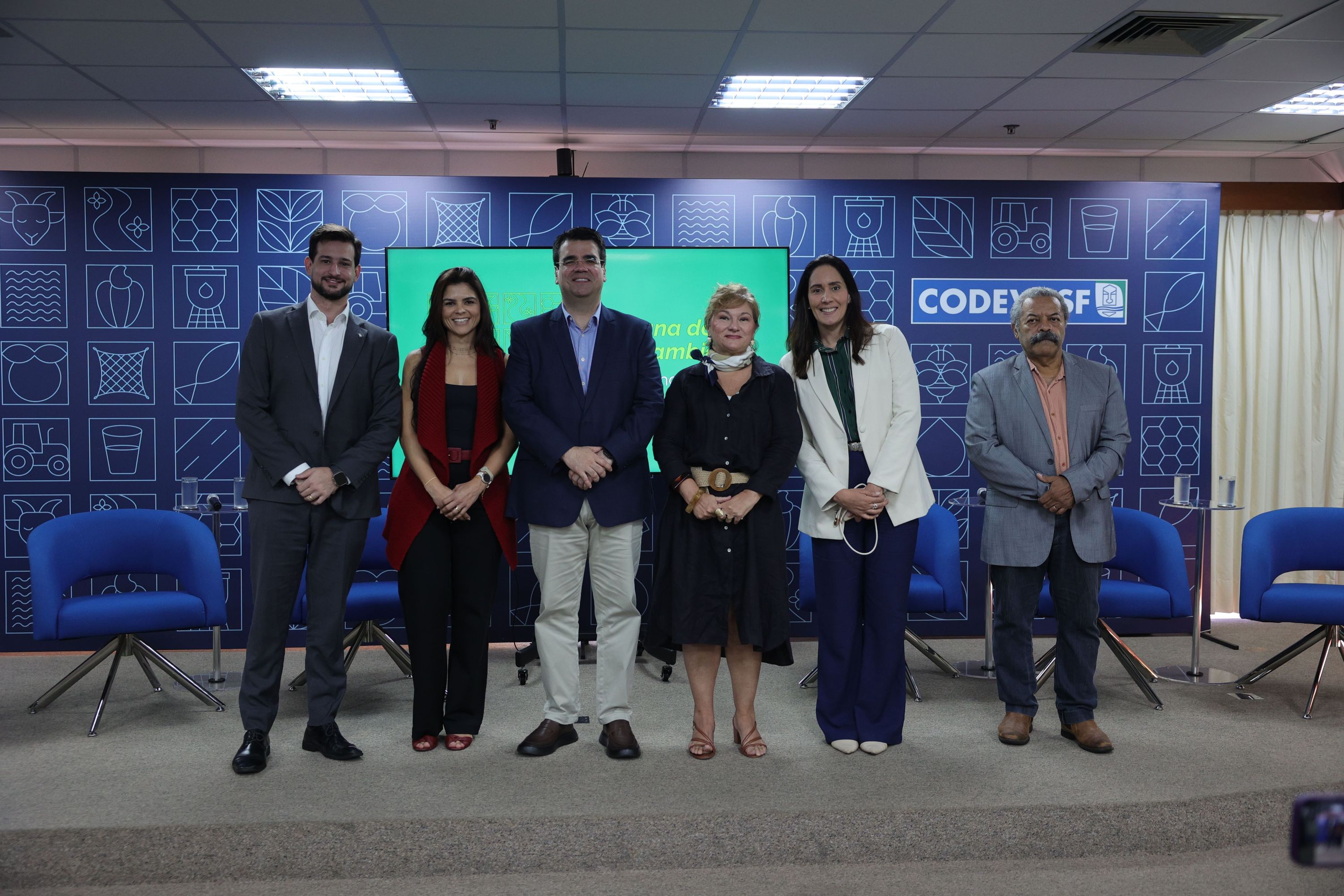 Seis pessoas em pé sobre palco com cadeiras azuis e painel da Codevasf ao fundo.