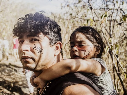 Imagem de indígena carregando uma criança nas costas