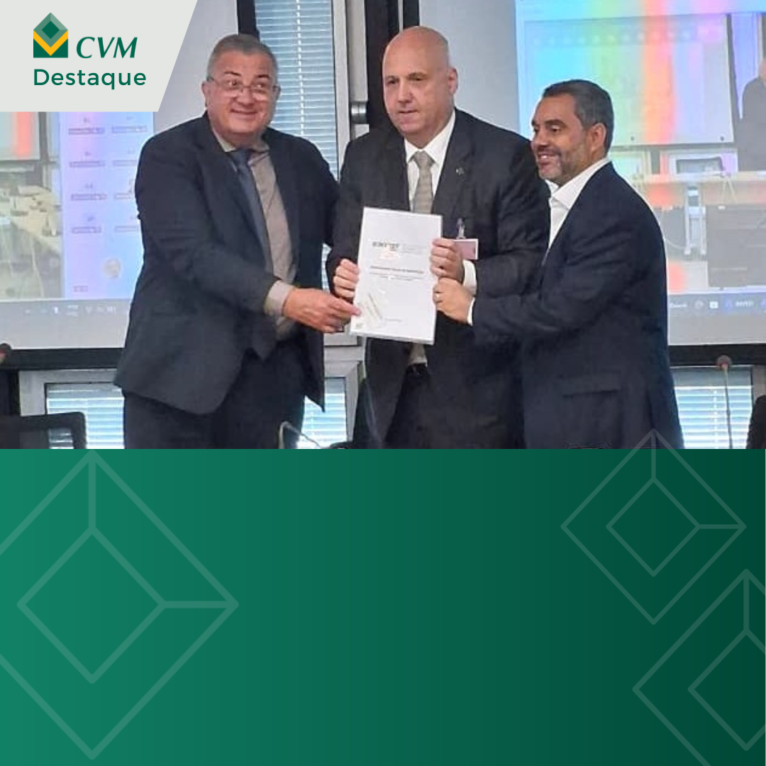 Três homens de terno exibem documento durante cerimônia em ambiente corporativo.