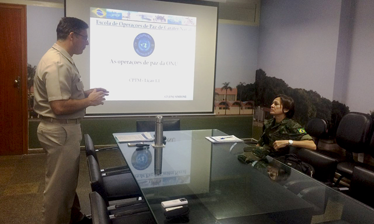 Maria Almeida sentada em uma sala de aula tendo instrução de um oficial que se encontra de pé