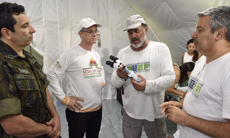 Representantes do Ministério da Defea, da SESAI e dos Expedicionários observam equipamento médico durante a visita as instalações de campanha