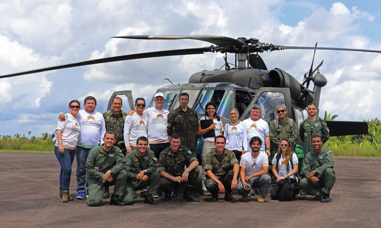 Militares e civis participantes do projeto SESAI em Ação posicionados em frente a um helicóptero da Força Aérea para uma foto 
