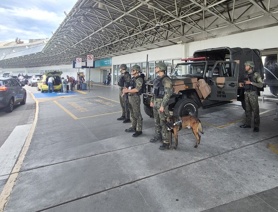 Militares uniformizados com um cão e uma viatura em área coberta de um terminal.