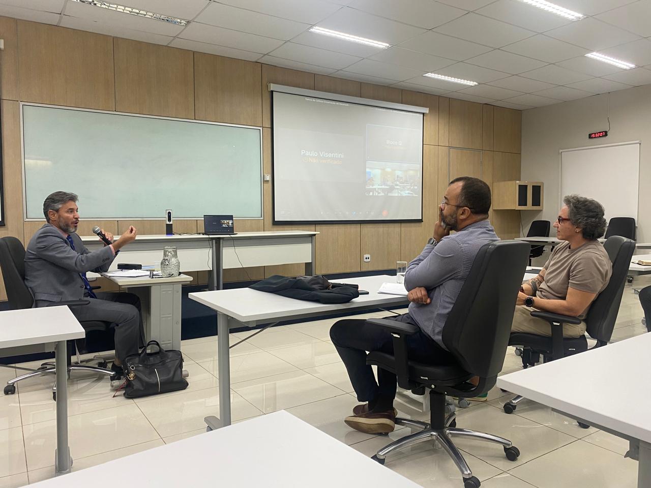 Mestrando apresentando sua dissertação para a banca. Ele está sentado em frente a 2 professores