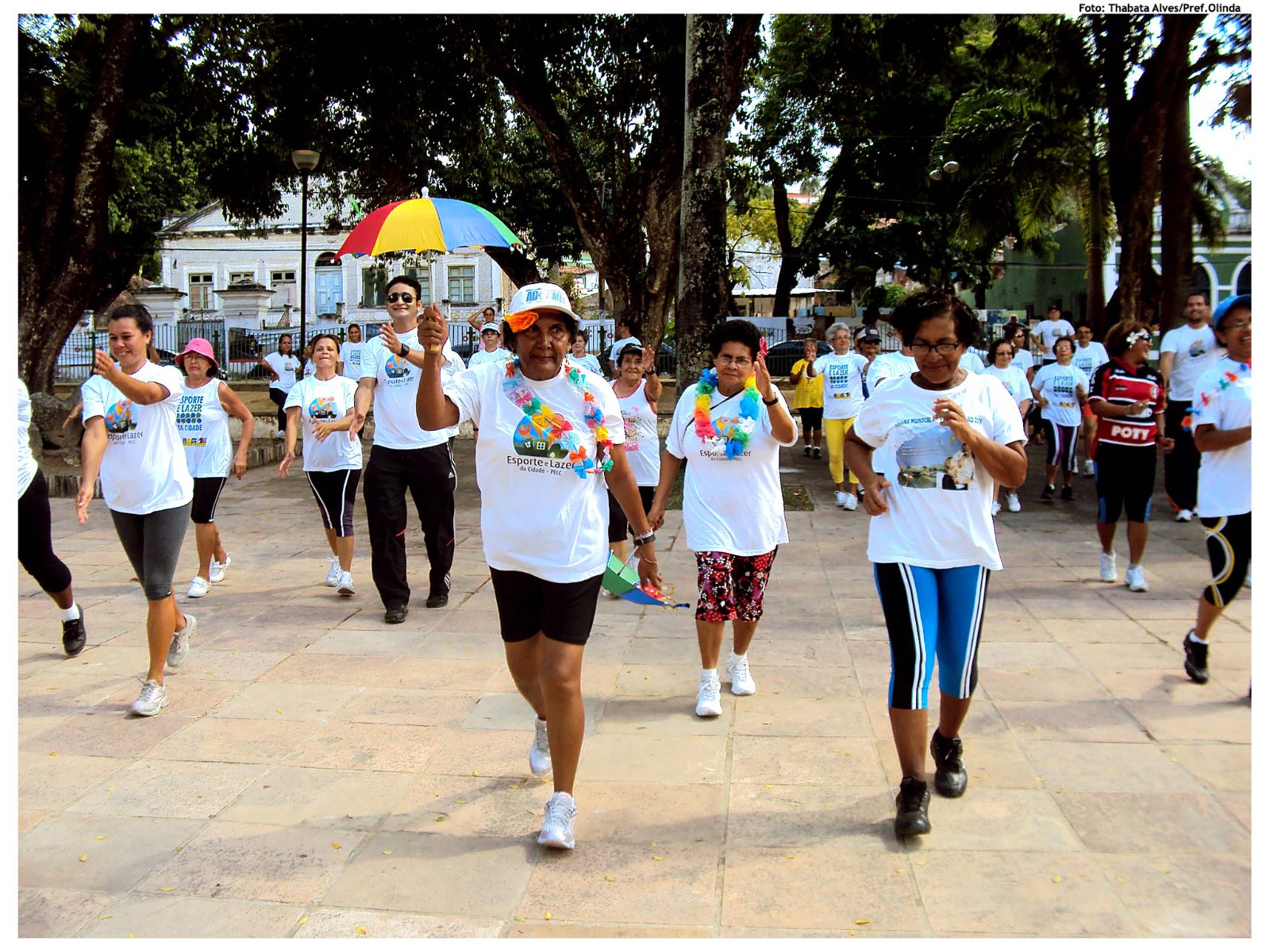 Grupo de pessoas caminha em parque usando camisetas brancas durante atividade coletiva ao ar livre