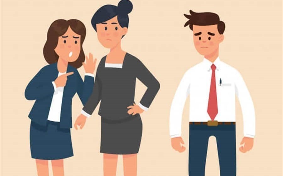 Duas mulheres, cochichando entre si, falam mal de um colega de trabalho, trocando comentários desprezativos sobre sua performance ou atitudes.