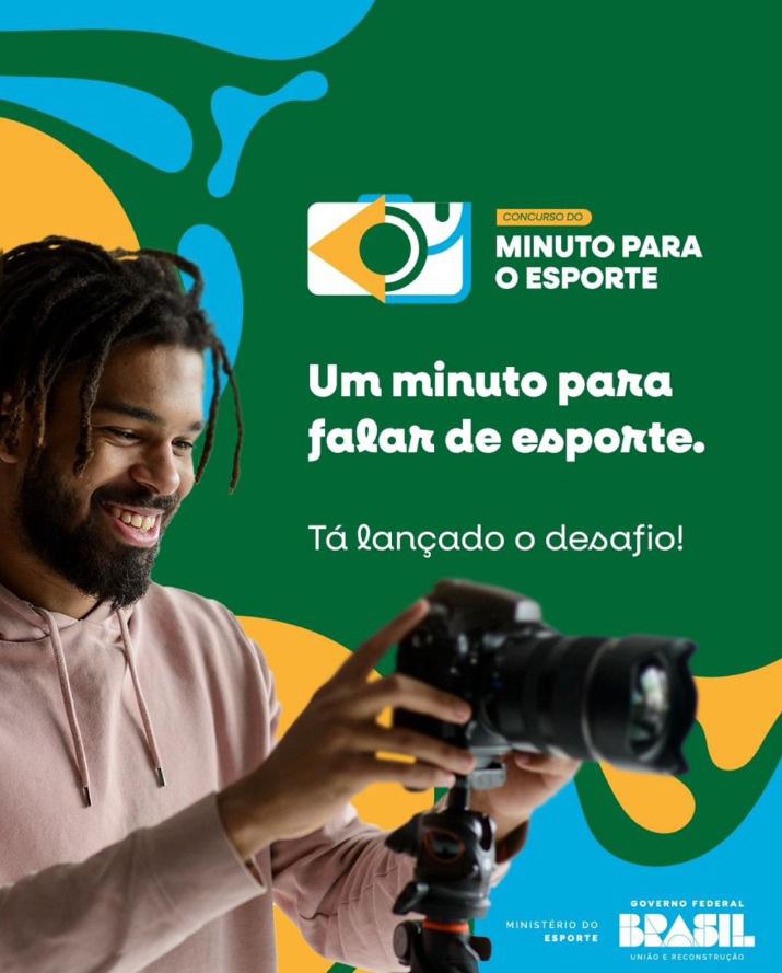 Homem sorrindo segura uma câmera. Fundo verde com formas azuis e amarelas. No topo está o logo do concurso Minuto para o Esporte. Texto: Um minuto para falar de esporte. Tá lançado o desafio! Logos do Ministério do Esporte e Governo Federal.