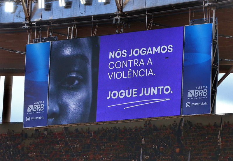 Telão mostra frame do vídeo de enfrentamento à violência contra as mulheres. 