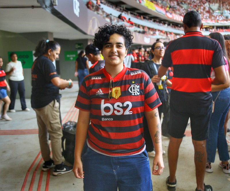 Torcedora com a camisa do Flamengo, cabelos pretos, cacheaados e curtos sorri para foto. 