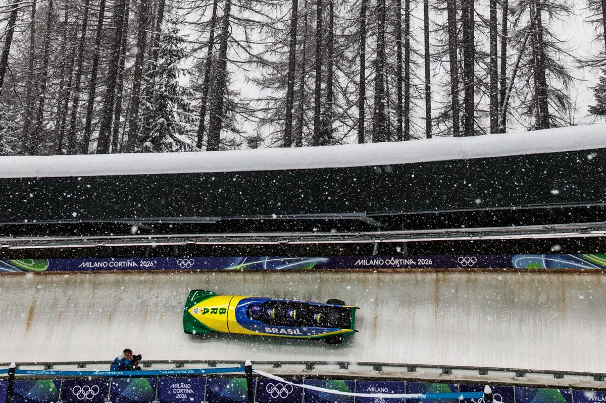 Atleta durante competição com carrinho de bosled e neve ao fundo.